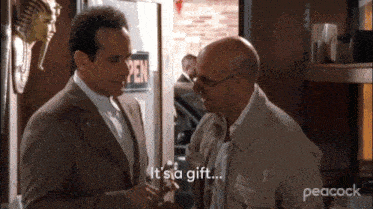 two men are talking in front of an open sign and one of them is saying it 's a gift